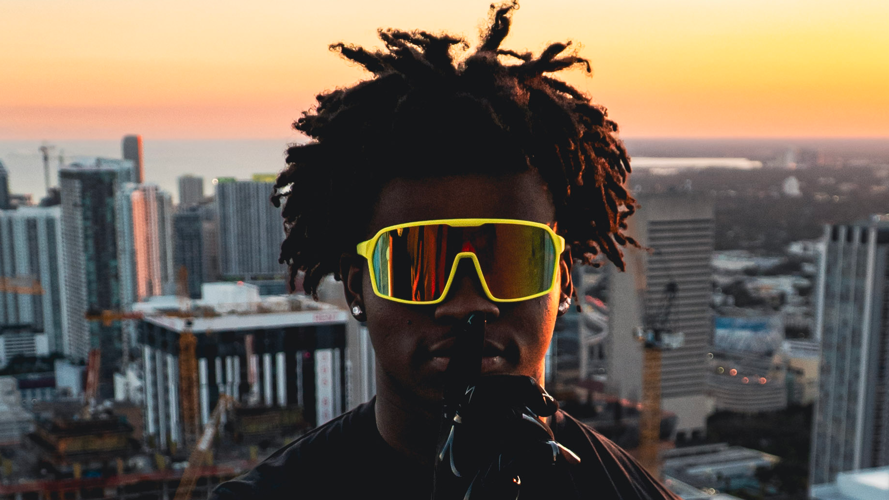 Person wearing sunglasses with a cityscape and sunset in the background