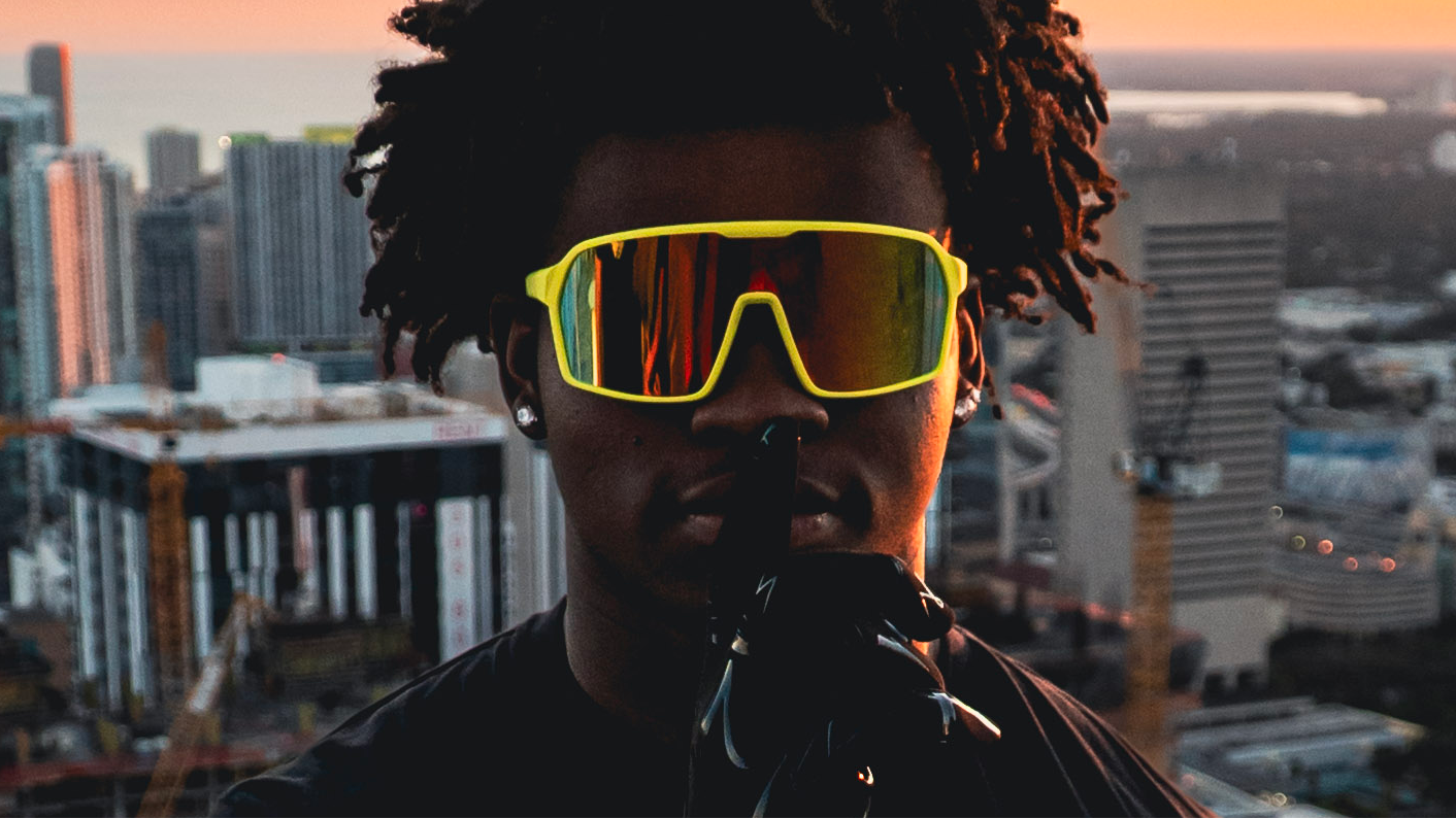 Person wearing sunglasses with a cityscape and sunset in the background